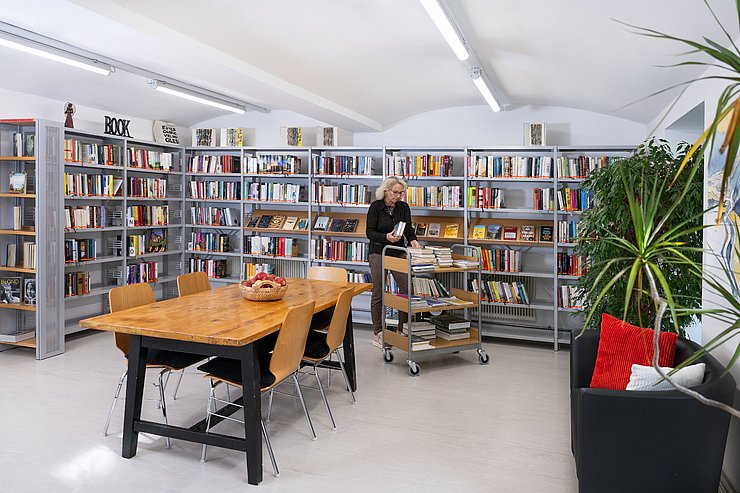 © Land Tirol/Birgit Pichler Photography Bibliothekarin sortiert Bücher in Bücherregal ein
