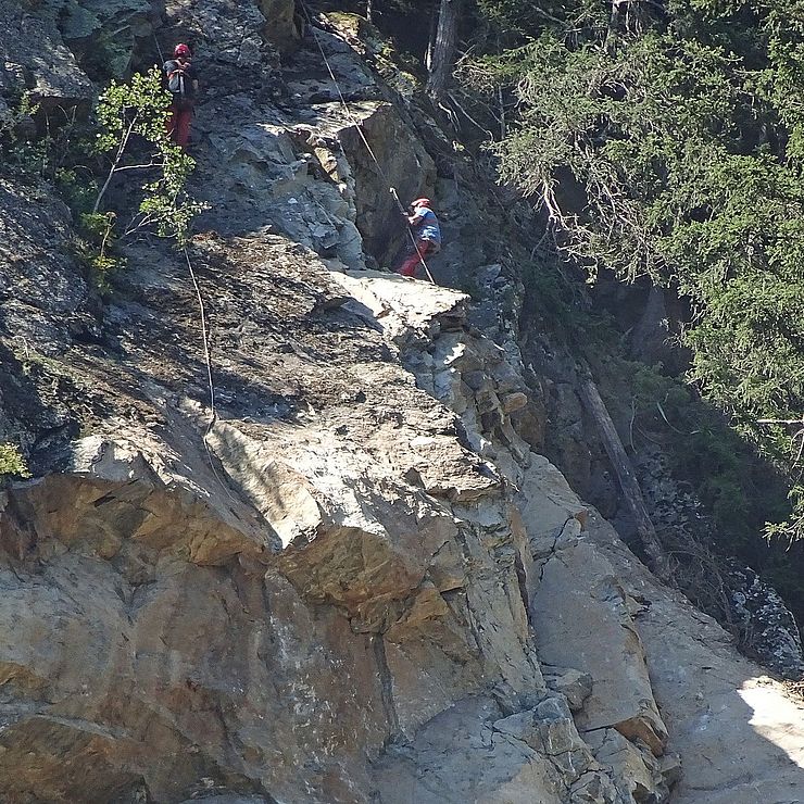 In einer steilen Felswand hängen zwei behelmte Arbeiter am Seil, die mit Felsberäumung beschäftigt sind.
