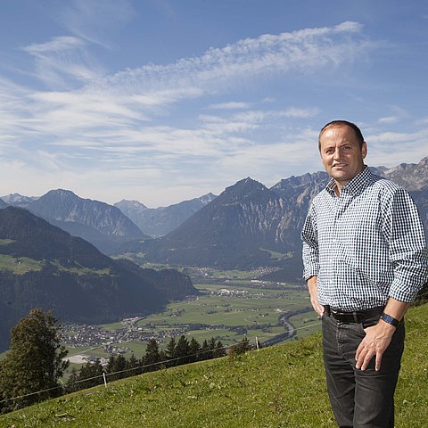Mann auf Wiese im Hintergrund ist ein Tal und Berge zu sehen