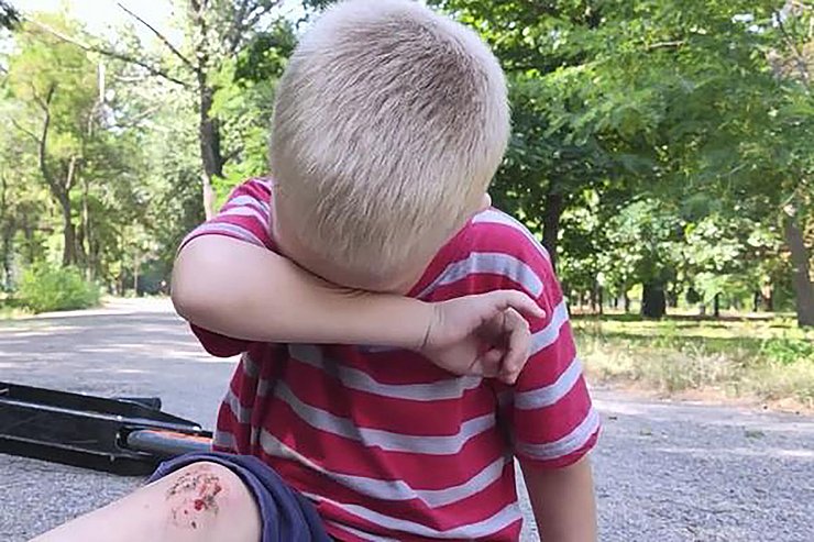 © FWU GmbH Ein kleiner Junge sitzt auf einer Straße, weinend und hat sich das Knie aufgerissen.