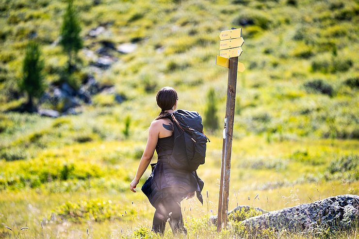 Eine Frau auf einem Wanderweg neben gelben Wegweisern