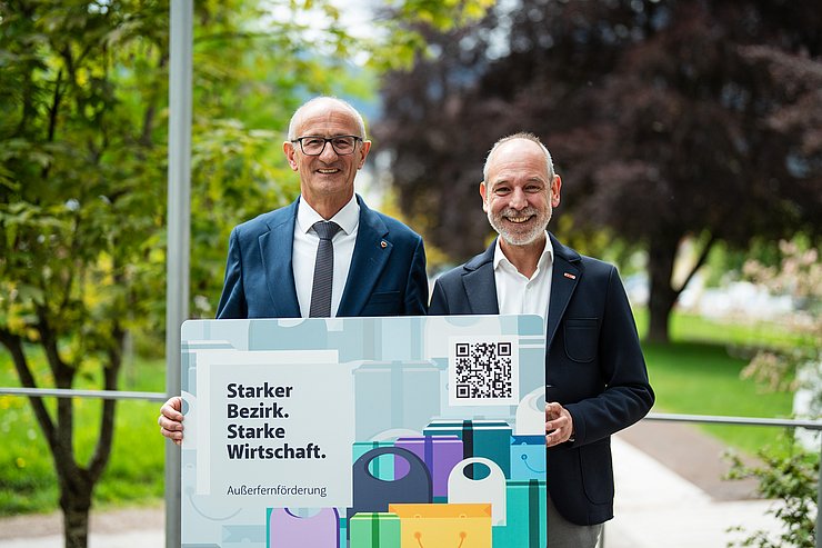 © Land Tirol/Fitsch Zwei Männer im Anzug halten einen großen Einkaufsgutschein.