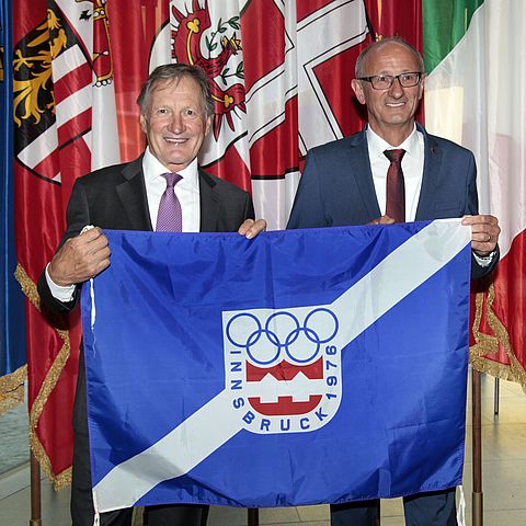 Franz Klammer steht links, daneben LH Anton Mattle: Beide halten im Landhaus ine originale Torflagge der Olympischen Winterspiele 1976.