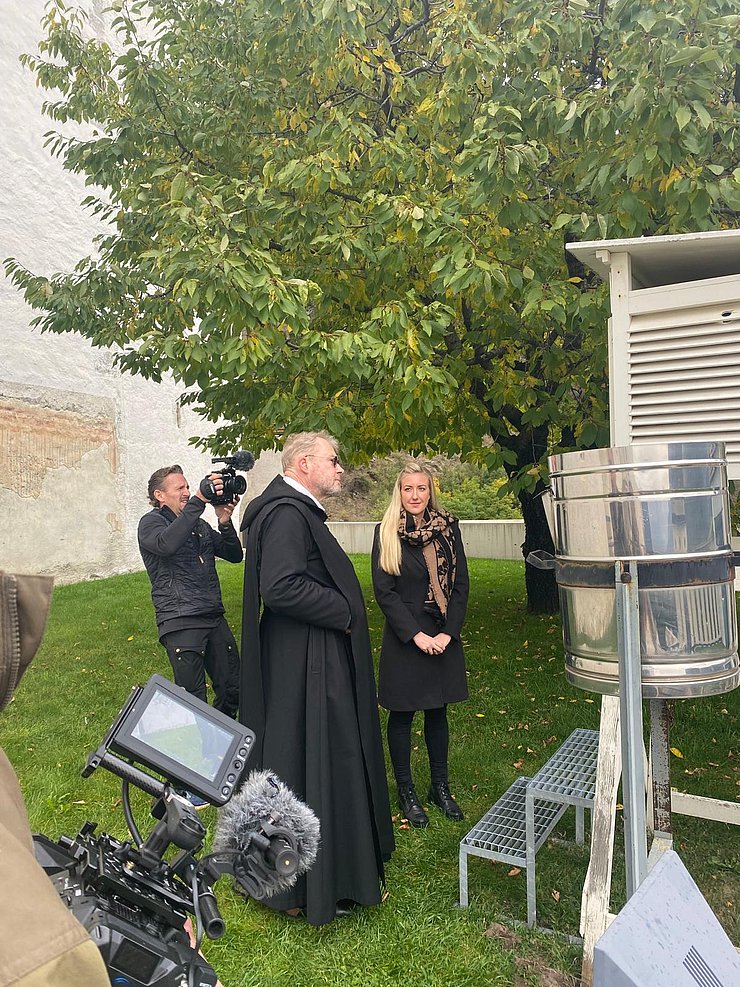 Personen stehen vor Wetterstation, Kamera zu sehen