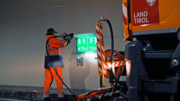 Mann spritzt mit Schlauch Fluchwegzeichen im Tunnel ab