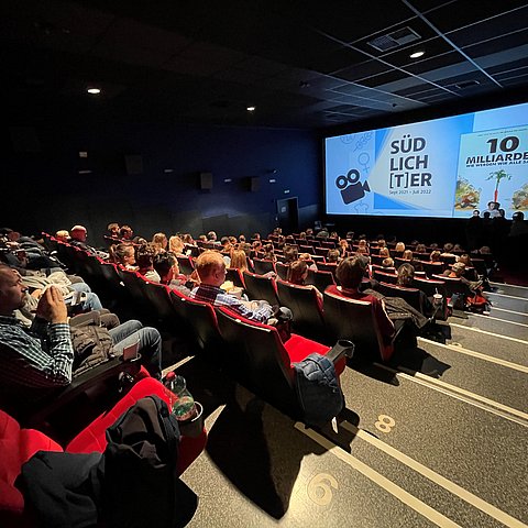 Voll besetzter Kinosaal, vorne auf der Leinwand: Titelbild des Films "10 Milliarden"