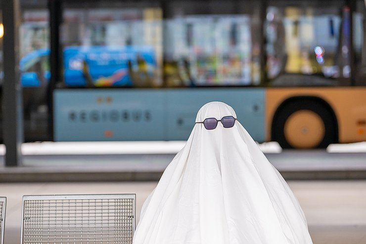 Mensch als Gespenst verkleidet an Bushaltestelle