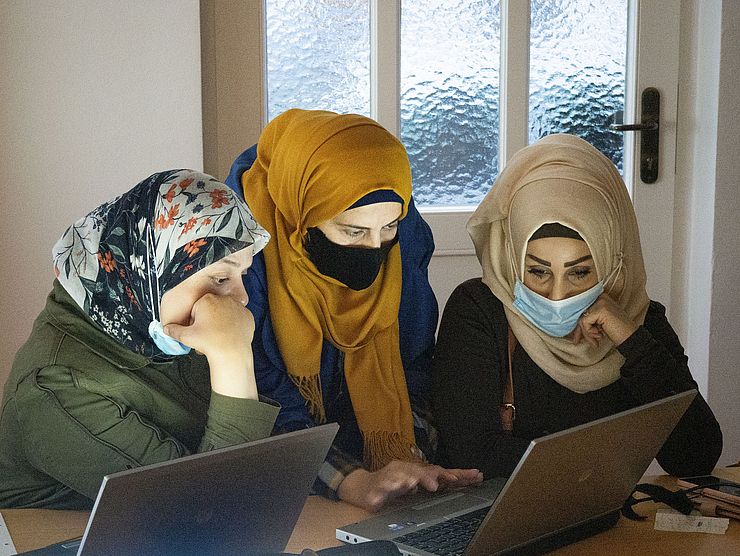 3 Frauen mit Kopftuch sitzen vor Laptop