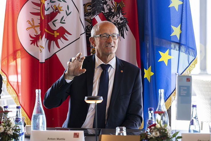 Landeshauptmann Anton Mattle beim Reden am Tisch. Im Hintergrund ist die Europäische und Österreichische Flagge zu sehen.