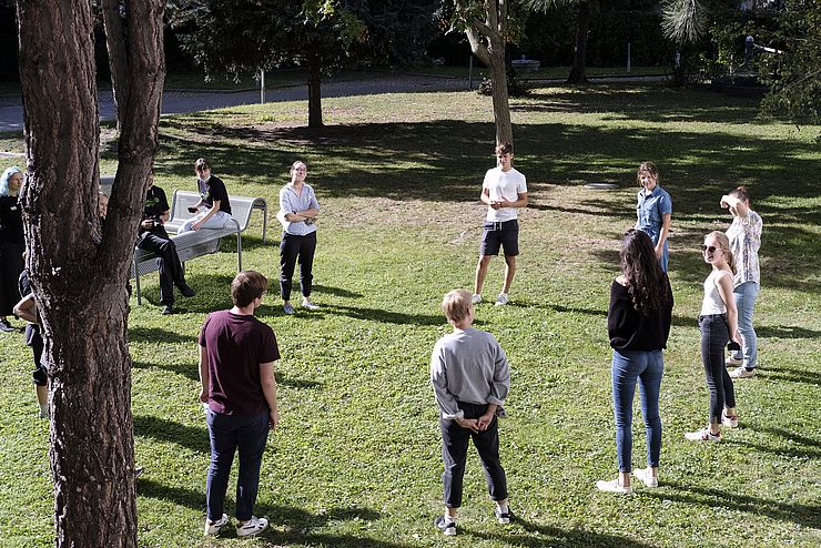12 Jugendliche stehen auf einer Wiese im Kreis