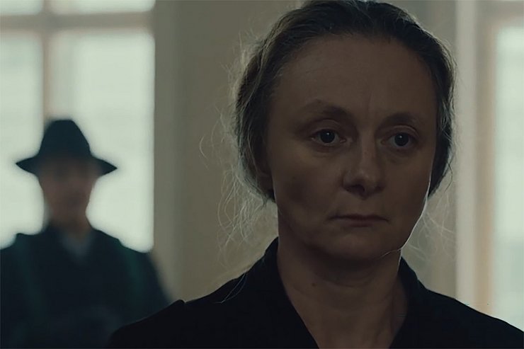 © Hoanzl Vertriebsges.m.b.H. Eine Frau im Mittelpunkt. Sie steht auf der rechten Seite des Bildes, wirkt ernst und im Ärger gefangen. Im Hintergrund, unscharf gehalten, steht ein Mann mit Hut und Mantel und sieht sie an.