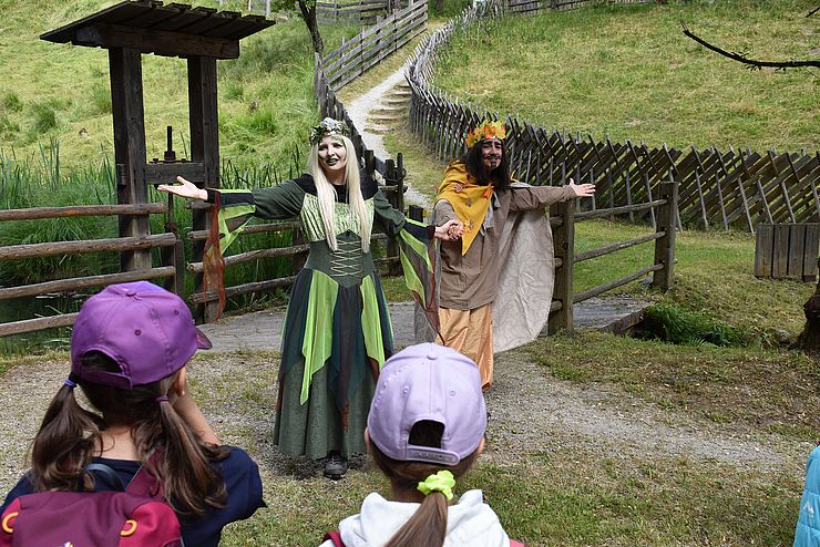 Zwei Märchenfiguren stehen auf einer Weggabelung und Kinder schauen ihnen beim Vorführen zu.