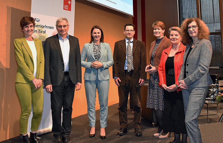 Zur Eröffnung der SeniorInnenenquete stehen in der Messehalle von links im Halbkreis: Karin Ziegner, SelbA, Demenzexperte Prof. Josef Marksteiner, LRin Astrid Mair, Altersforscher Prof. Marc Luy, Angelika Stegmayr, Erwachsenenbildung Diözese Innsbruck, Moderatorin Pia Krismer und Ines Bürgler, Vorständin Landesabteilung Gesellschaft und Arbeit.