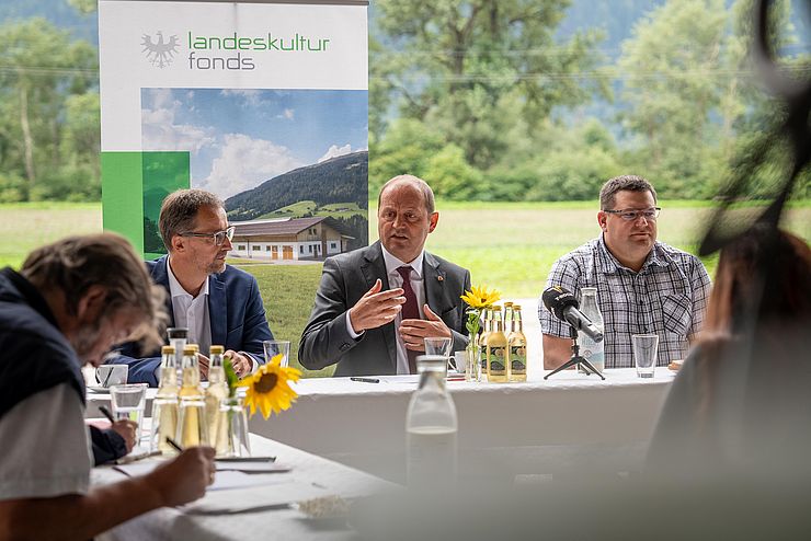 Im Bild sind Thomas Danzl, Geschäftsführer Landeskulturfonds, Landwirtschaftsreferent LHStv Josef Geisler und Georg Kapferer  bei der Pressekonferenz zu sehen. Sie sitzen um einen weißen Tisch im Garten.