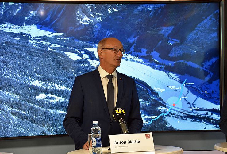 LH Anton Mattle steht bei der Pressekonferenz hinter einem weißen Tisch. Im Hintergrund sieht man eine Landkarte der Region.