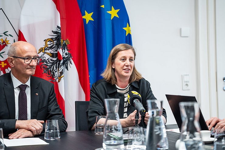 Zwei Personen sitzen an einem Tisch vor Fahnen