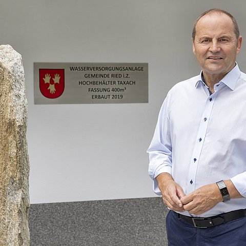 Mann steht im Bild, dahinter ein Schild einer Wasserversorgungsanlage