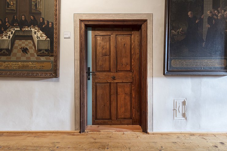Eine Holztür und zwei an der Wand hängende Bilder sind zu sehen.