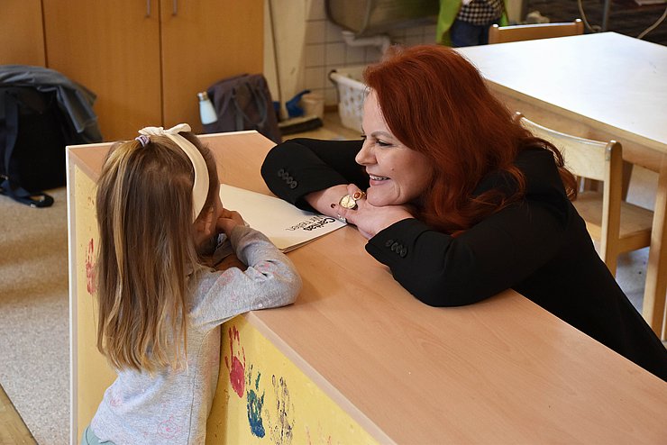 Foto von einer Frau die über ein Regal gebeugt mit einem Mädchen spricht.