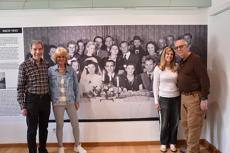 © Land Tirol/Neuner Zwei Paare stehen vor einem schwarz-weiß Familienfoto, das an der Wand hängt.