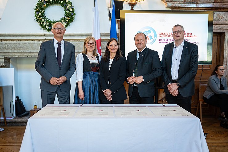 Personen stehen nebeneinander hinter Tisch mit Urkunden